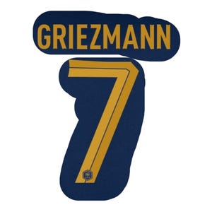 May include: A navy blue patch with the name "Griezmann" in gold lettering above a gold number "7". The number has gold stripes and a small emblem at the bottom. The patch is designed for sports apparel.