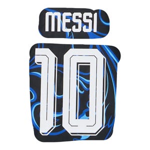 Może przedstawiać: Czarny i niebieski przedmiot sportowy z napisem "MESSI" białymi literami blokowymi nad dużą białą liczbą "10". Biała liczba ma czarny kontur na czarnym tle z niebieskimi wzorami w kształcie płomieni.