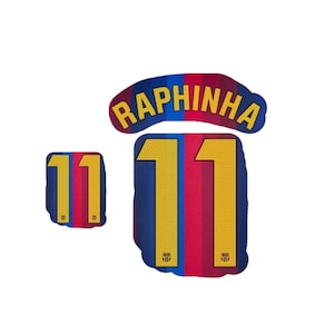 Pode incluir: Um conjunto de transferências termocolantes com o nome RAPHINHA em letras amarelas e o número 11 em amarelo com um padrão texturizado. O design inclui riscas verticais azuis e vermelhas e o emblema do FC Barcelona na base do número 11.