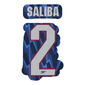 May include: A navy blue and white jersey patch with the name "SALIBA" above a number "2". The number is white with a red outline, set against a navy blue background with a lightning bolt pattern. A small logo is at the bottom.