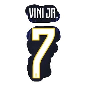Puede incluir: Gráfico azul marino con el nombre "VINI JR." encima del número "7". El número es blanco con un contorno dorado, sobre un fondo azul marino. El diseño es probablemente para ropa deportiva.