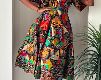 May include: A woman wearing a colorful, geometric patterned midi dress with puffed sleeves and a plunging neckline. She is wearing black sunglasses and clear heels.