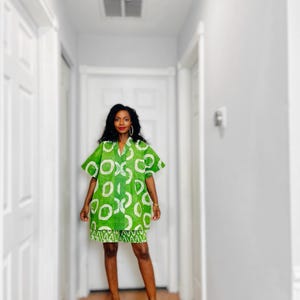 May include: A green and white patterned dress and matching skirt. The dress has short sleeves and a collared neckline. The skirt has a white zigzag pattern at the hem. The person is wearing red high heels.