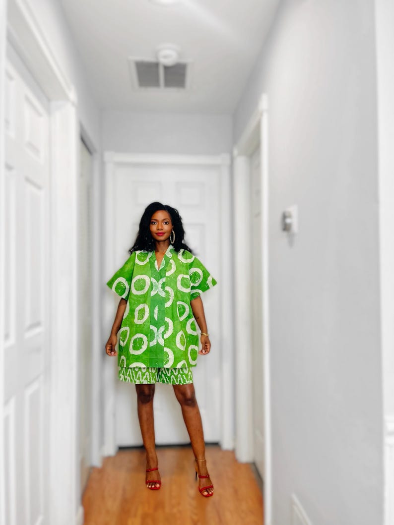 May include: A green and white patterned dress and matching skirt. The dress has short sleeves and a collared neckline. The skirt has a white zigzag pattern at the hem. The person is wearing red high heels.
