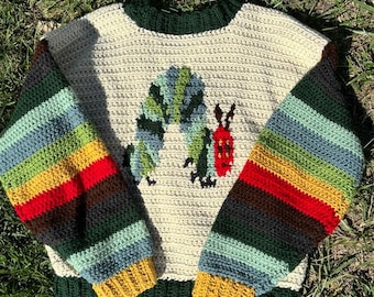 May include: A cream-colored crochet sweater featuring a colorful caterpillar design on the front. The sleeves have horizontal stripes in various colors, including green, blue, yellow, and red. The collar and cuffs are dark green and yellow.