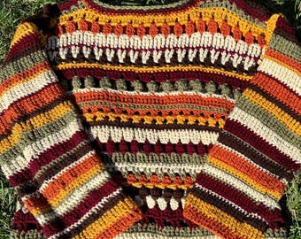 May include: A crocheted sweater with a striped pattern in shades of red, orange, yellow, green, and brown. The sweater has a round neckline and long sleeves.