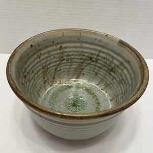 May include: A white ceramic bowl with brown and green glaze. The bowl has a rounded shape and a slightly flared rim.