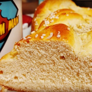 May include: A close-up of a loaf of bread with a golden brown crust and a sprinkle of sugar crystals on top. The bread is sliced and shows a soft, fluffy interior.