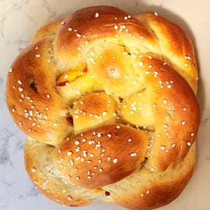 May include: A golden-brown, braided loaf of bread, sprinkled with white sugar crystals. The bread has a glossy finish and is baked to a rich, even color. The bread is a traditional baked good.
