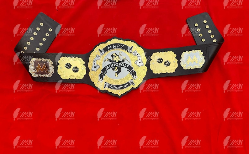 May include: A black and gold championship belt with a Monopoly themed center plate. The center plate features the Monopoly Man character and the text "MNPY MONOPOLY CHAMPION".