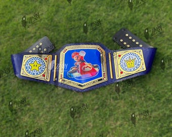 May include: A blue and gold championship belt featuring a Mario Kart design. The belt has a central emblem with Mario in a kart, flanked by star and crown emblems. The text "MARIO KART CHAMPION" is displayed.