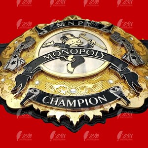 Może przedstawiać: Złoty i czarny pas mistrzowski z logo Monopoly Man i napisem "MONOPOLY CHAMPION".