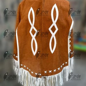 May include: A brown suede poncho with white geometric designs and fringe trim. The poncho features white accents along the edges and a series of white fringe at the bottom. The design includes two large, stylized white infinity symbols.