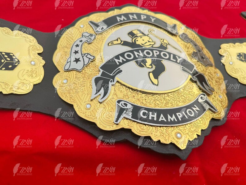 May include: A gold and black championship belt with a Monopoly theme. The belt features a silver center plate with a Monopoly Man figure, the words "MONOPOLY" and "CHAMPION", and a dice design on the side.