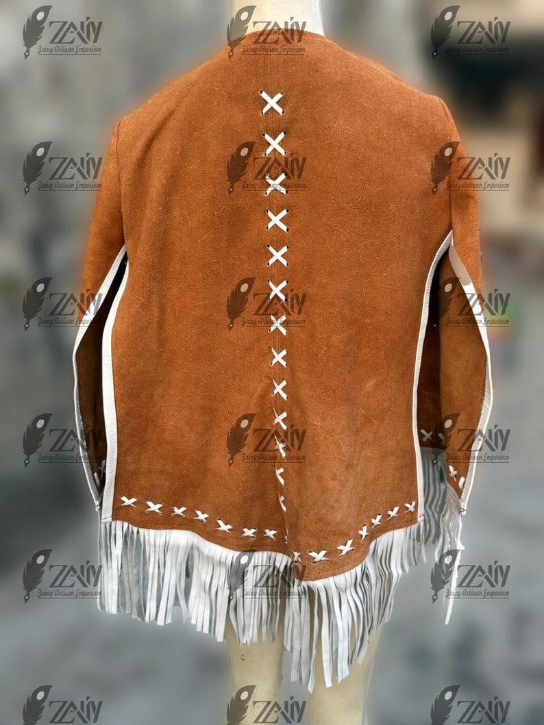 May include: A brown suede jacket with white fringe and trim. The back of the jacket features white cross-stitch detailing down the center and along the bottom edge. The jacket has a classic, rustic design.