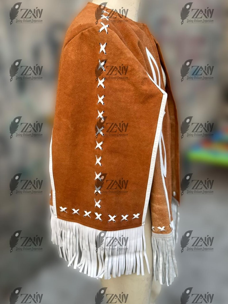 May include: A brown suede jacket with white fringe and accents. The jacket features white stitching and trim, with a fringe detail along the bottom. The jacket is displayed on a mannequin.