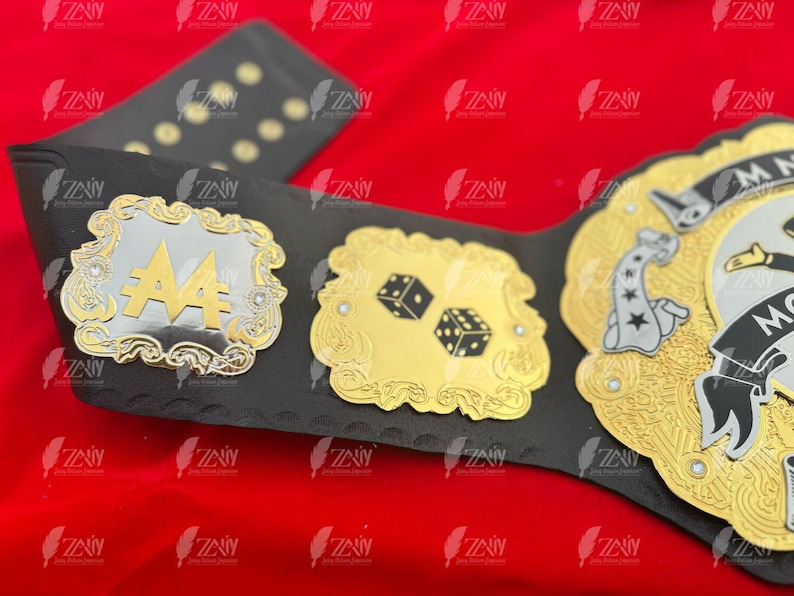 May include: A black leather championship belt with gold and silver accents. The belt features a large, ornate silver plate with the number "4" in the center. The belt also has a smaller gold plate with two dice and a larger gold plate with a stylized image of a person holding a playing card.