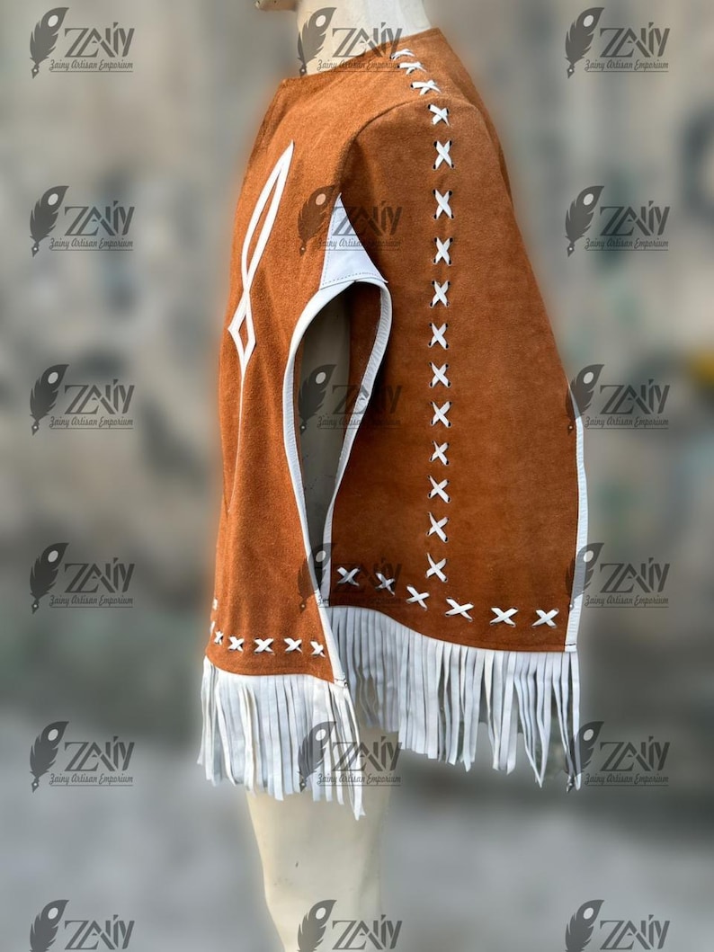 May include: A brown suede vest with white accents and fringe. The vest features white stitching and a geometric design on the front. The edges are trimmed with white leather and fringe. The vest is displayed on a mannequin.
