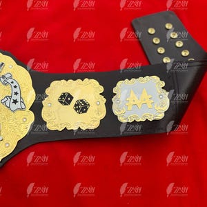 May include: A black leather championship belt with gold and silver accents. The belt features a large, ornate buckle with the word "MONOPOLY" and a dice design. There are two smaller plates on the belt, one with a dice design and the other with the letters "AA".