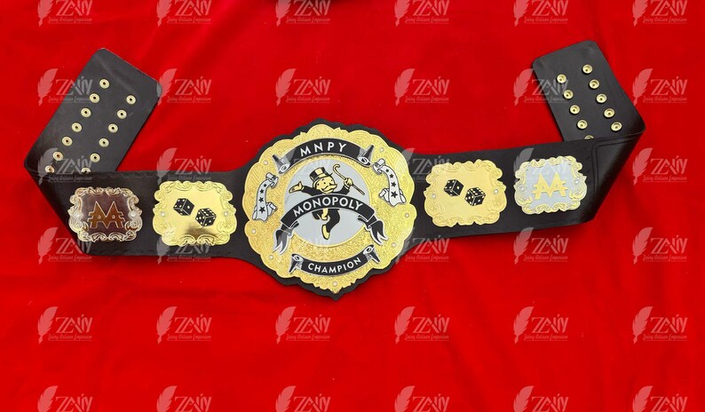 May include: A black and gold championship belt with a Monopoly theme. The center plate features a Monopoly man figure and the words "MONOPOLY CHAMPION".