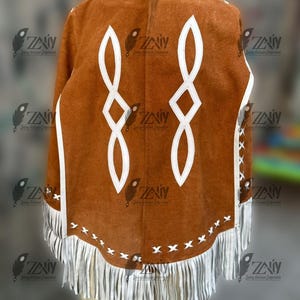 May include: A brown suede poncho with white geometric designs and fringe trim. The poncho features white accents along the edges and decorative stitching. The design includes a series of white, stylized infinity symbols.