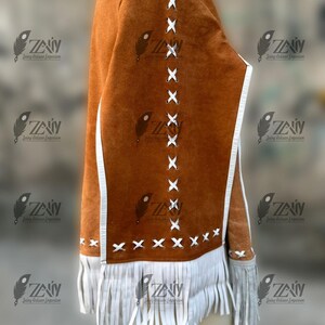 May include: A brown suede jacket with white fringe and accents. The jacket features white stitching details and a white trim. The sleeves have fringe at the cuffs. The jacket is a unique piece of apparel.