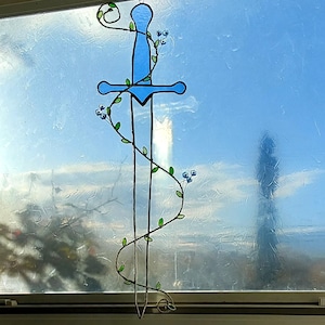 May include: A stained glass window art piece depicting a blue sword with a vine of green leaves and blue flowers wrapping around it.