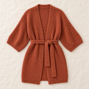 May include: A rust-colored open-front cardigan featuring a textured knit pattern, three-quarter length sleeves, and a matching tie belt at the waist. The garment has a ribbed collar and ribbed cuffs, providing a structured look with a consistent knit.