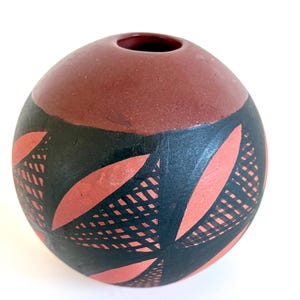Peut inclure: Un vase sphérique en terre cuite avec une partie supérieure lisse et unie brun-rouge et un corps inférieur orné d'un motif répétitif de formes en feuilles peintes en noir et de triangles hachurés sur la surface en argile brun-rouge naturelle.