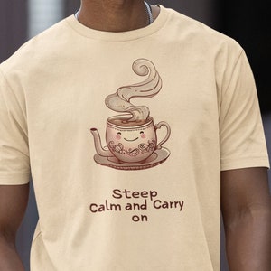 May include: A beige t-shirt with a cartoon illustration of a steaming teacup with a smiling face. The text "Steep Calm and Carry on" is printed below the illustration.