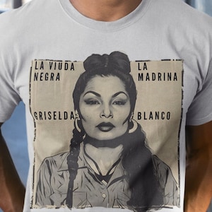 May include: A gray t-shirt with a black and white image of a woman with the text "La Viuda Negra La Madrina Griselda Blanco" printed on the front.