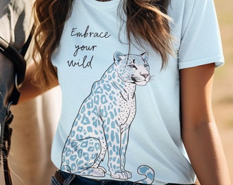 Könnte beinhalten: Hellblaues T-Shirt mit Leopardenmuster und dem Text "Embrace your wild". Der Leopard hat blaue Flecken. Die Person trägt einen weißen Cowboyhut und blaue Jeans.