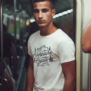 Puede incluir: Una camiseta blanca con un gr&aacute;fico negro de monta&ntilde;as y &aacute;rboles. El gr&aacute;fico dice "Adventure Awaits".