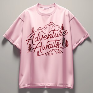 Puede incluir: Camiseta rosa de manga corta con un dise&ntilde;o gr&aacute;fico rojo de monta&ntilde;as y &aacute;rboles. El texto "Adventure Awaits" est&aacute; impreso en rojo en la camiseta.