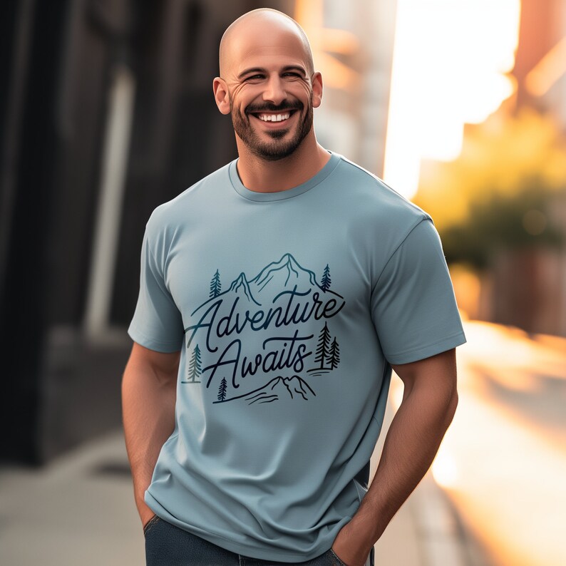 Puede incluir: Una camiseta azul claro con un dise&ntilde;o gr&aacute;fico de monta&ntilde;as y &aacute;rboles. El texto "Adventure Awaits" est&aacute; impreso en la camiseta.