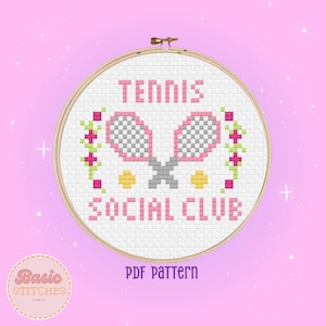 Könnte beinhalten: Ein weißes Kreuzstichmuster mit rosa Schriftzug, der "Tennis Social Club" lautet. Das Muster zeigt zwei rosa und graue Tennisschläger mit gelben Tennisbällen und rosa und grünen floralen Akzenten. Das Muster wird in einem hölzernen Stickrahmen angezeigt.