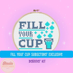 May include: A cross-stitch pattern in a wooden embroidery hoop with the text "FILL YOUR CUP" in blue and teal. The pattern includes a blue cup with teal water pouring out. The text "FILL YOUR CUP SUBSCRIBER EXCLUSIVE BEGINNER KIT" is below the hoop.