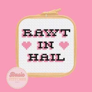 May include: A white cross-stitch embroidery hoop with the text "RAWT IN HAIL" in black and pink lettering with two pink hearts on either side of the word "IN".