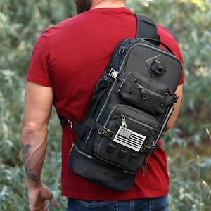 May include: A black tactical sling backpack with multiple pockets and straps. The backpack has a small American flag patch attached to the front.