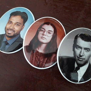 May include: Three round, white-rimmed, ceramic coasters with images of people. The first coaster features a man with dark hair and a beard wearing a dark suit and a light blue shirt. The second coaster features a woman with long dark hair wearing a red sweater. The third coaster features a man with dark hair wearing a dark suit and a white shirt with a patterned tie.