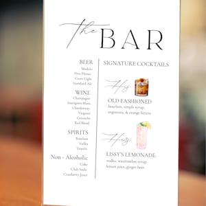 May include: A clear acrylic bar menu with the words "The BAR" in elegant script. The menu lists beer, wine, spirits, and non-alcoholic beverages. Signature cocktails include an Old Fashioned and Lissy's Lemonade.