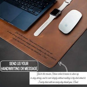 May include: A brown leather desk mat with a laptop, a white Apple Watch, and a white Apple mouse. The mat has engraved text and a white box that says "SEND US YOUR HANDWRITING OR MESSAGE".
