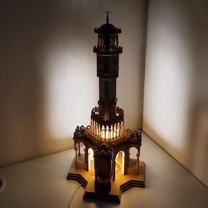 Puede incluir: Modelo de madera detallado de una mezquita con un minarete, iluminado desde dentro. El intrincado diseño presenta arcos y una base en forma de estrella. La luz cálida crea un ambiente acogedor. Un cable de alimentación sale de la base.
