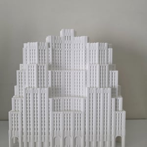 May include: A white architectural model of a tiered skyscraper with intricate details. The model features multiple levels, arched entryways, and vertical lines, creating a detailed representation of a building.