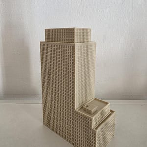 Könnte beinhalten: Ein beigefarbenes, 3D-gedrucktes Architekturmodell eines Wolkenkratzers mit abgestuftem Design. Die Struktur weist ein Gitter aus quadratischen Fenstern an den Außenwänden, einen flachen Dachabschnitt und einen kleinen rechteckigen Block auf.