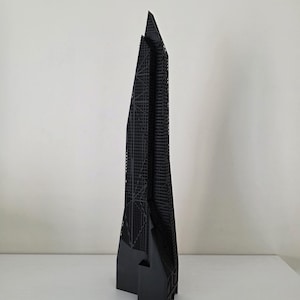 May include: A black architectural model of a skyscraper with a distinctive, angular design. The model features intricate detailing, showcasing the building's structural framework. The skyscraper stands tall against a plain white background, emphasising its geometric form.