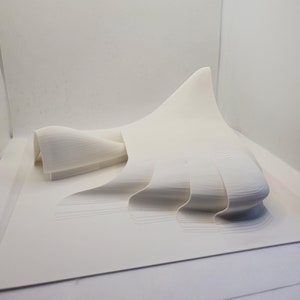 Może przedstawiać: Biały model budynku wydrukowany w 3D o płynnym, organicznym designie. Model znajduje się na białej powierzchni.