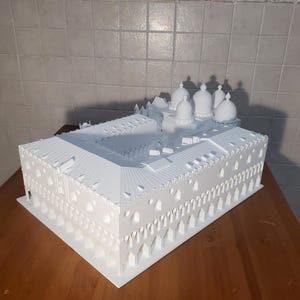 May include: A white 3D printed model of a building with multiple domes. The model is detailed and intricate, with arches and windows.