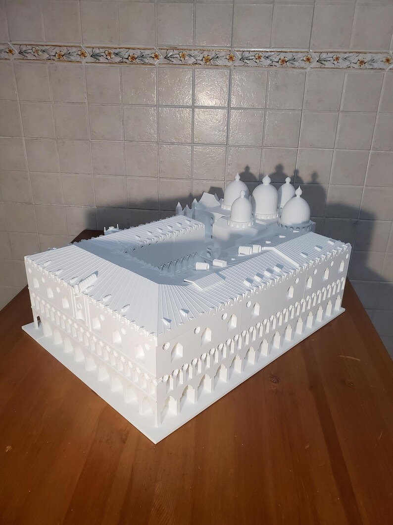 May include: A white 3D printed model of a building with multiple domes. The model is detailed and intricate, with arches and windows.