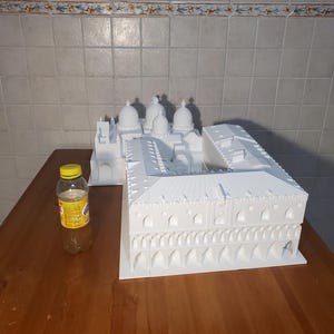 May include: A white 3D printed model of a building with multiple domes and a large courtyard. The model is sitting on a wooden table.